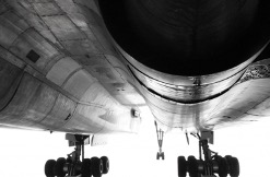 The long underbelly of an airplane, which has two undulations for engines, and the landing gear down against a completely white backdrop giving the image a classic black & white feel.