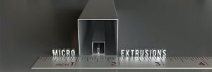: The word “microextrusions” reflects on a metal ruler up to the 4-inch mark, with 3 sizes of square hollow-shaped miniature extrusions lined up against the 1-2-inch marks.