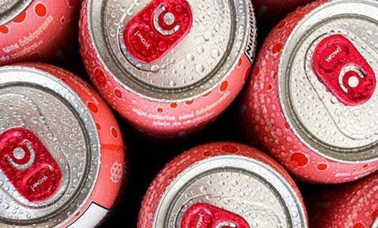 A photograph of the top of a cluster of red, aluminum canned drinks, with condensation droplets forming all over the cans.