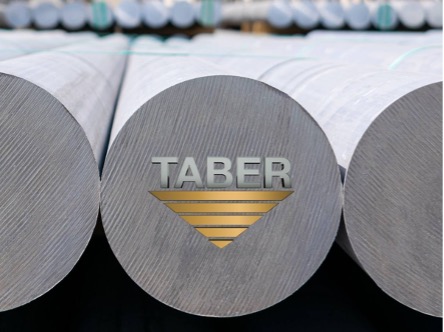 Close-up shot of the Taber logo, the letters Taber in “metal” gray and triangular metal gold logo beneath, centered and overlayed on the end of center round aluminum billets in the foreground, several more rounds blurred in the background.