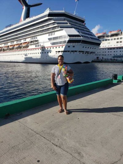 Taber Extrusions' In Focus Spotlight Ashley Johnson, customer service rep, standing in front of water and cruise ships wearing striped shirt and blue shorts