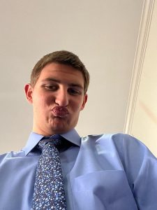 David Jackson's son, a young man in a blue shirt and tie making a face pursing lips