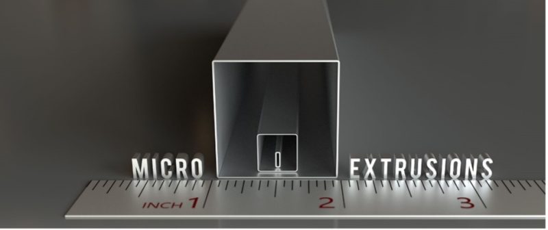 A large metal extrusion profile with 3 hollow pieces nested inside the other. On either side of the extrusions are the words “MICRO” and “EXTRUSIONS” runs along the length of a 3-inch section of a ruler.