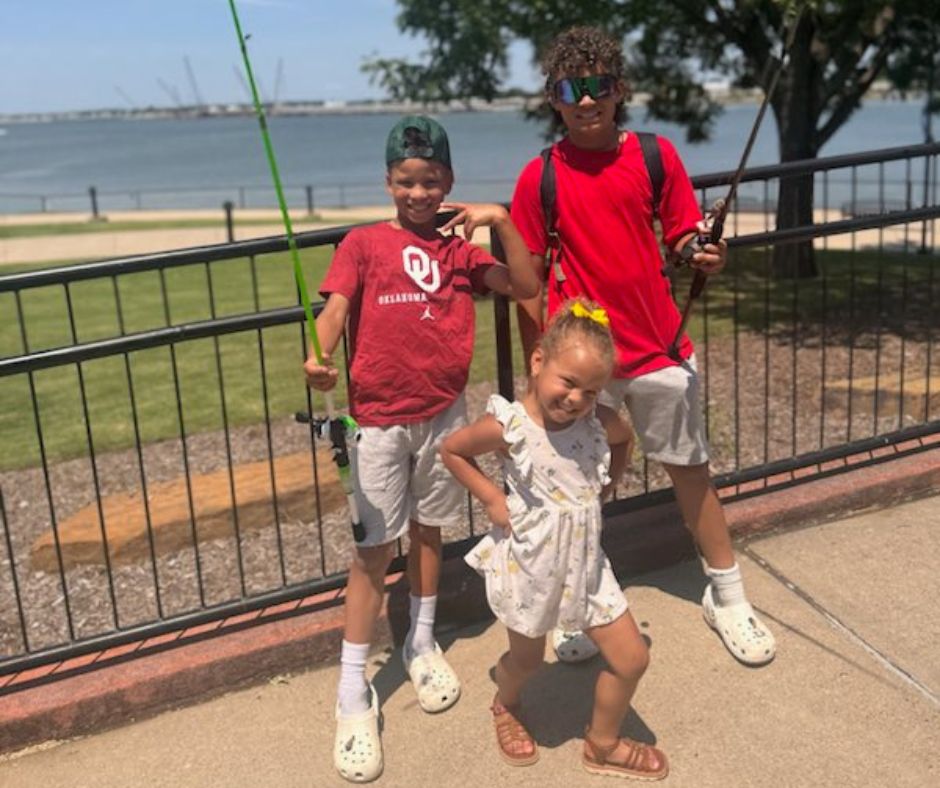 A photo of JP's three kids smiling in front of a lake. The two boys, Kaden and Asher, are holding fishing poles and his daughter, Savvy, is posing between them.