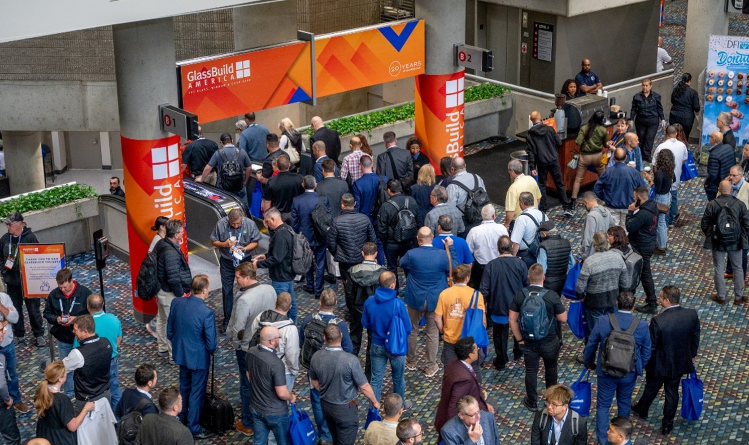 A crowd of people attending GlassBuild America, showcasing the entrance area with event banners and attendees gathered.