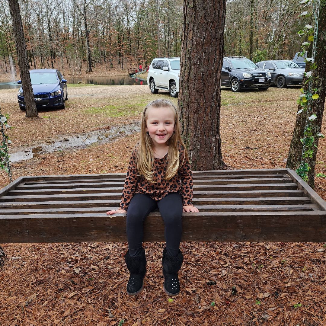 An adorable photo of Regina Tramel's granddaughter smiling on a bench.
