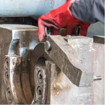 An operator with safety gloves places a profile die inside an aluminum extrusion press